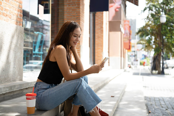 Smiling Asian woman sitting on stairs using smart phone. - Photo, Image