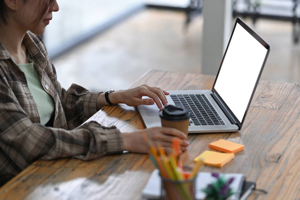 Female freelancer holding coffee cup and working with computer laptop on wooden table. - Photo, Image
