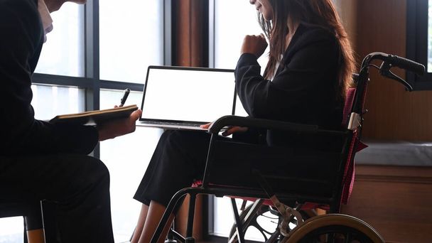 Zakenvrouw met een handicap in een rolstoel werkt samen met haar collega 's. - Foto, afbeelding