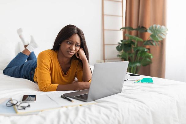 Чорна жінка незадоволена Дивлячись на ноутбук Комп'ютер лежить в спальні
 - Фото, зображення