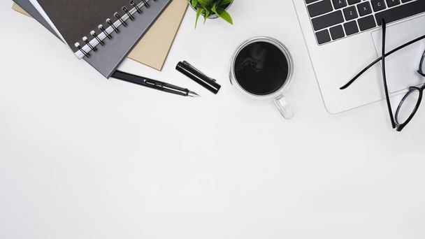 Escritorio de oficina blanco con computadora portátil, anteojos, taza de café y libro. Vista superior. - Foto, Imagen