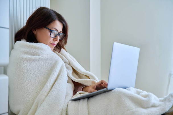Mulher trabalhando em casa com laptop, aquecendo com cobertor e radiador de aquecimento - Foto, Imagem