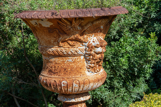Pot en métal vide, avec des figures sculptées dans le métal, avec un fond vert de plantes. - Photo, image