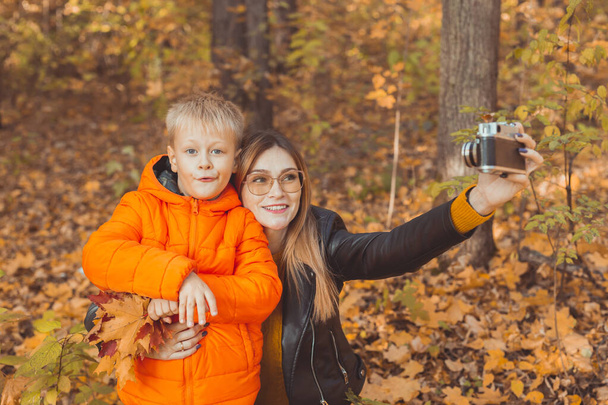 Son and mother are taking selfie on camera in autumn park. Single parent, leisure and fall season concept. - Foto, imagen