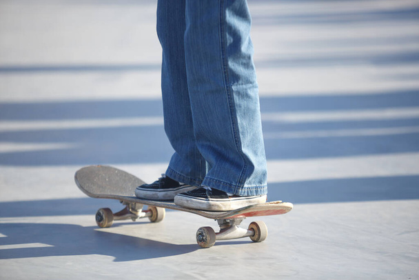 Skater kid rides on skateboard in outdoor concrete skatepark in sunny day - Photo, image