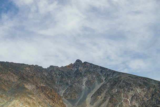 Όμορφο τοπίο με ηλιοφωτισμένο ψηλό κορυφές βουνών κορυφές σε πορτοκαλί χρώματα του φθινοπώρου κάτω από σύννεφα cirrus σε μπλε ουρανό. Πολύχρωμο αλπικό τοπίο με φοβερό βουνό κορυφή στη χρυσή ηλιοφάνεια κάτω από συννεφιασμένο ουρανό - Φωτογραφία, εικόνα