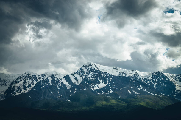 Драматический горный пейзаж с большим снежным горным хребтом под облачным небом. Темно-атмосферные горные пейзажи с высоким горным хребтом в пасмурную погоду. Огромные горы под серыми облаками. - Фото, изображение
