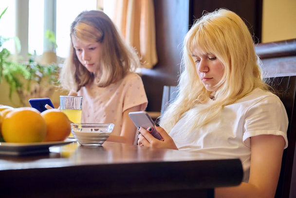Children two girls sisters eating at home, looking at smartphones - Φωτογραφία, εικόνα