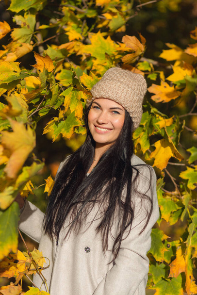 Portrait of a joyful young woman enjoying in the autumn park. Beautiful brunette girl in autumn grey coat and knitted hat. Relax in nature. High quality photo - Foto, imagen