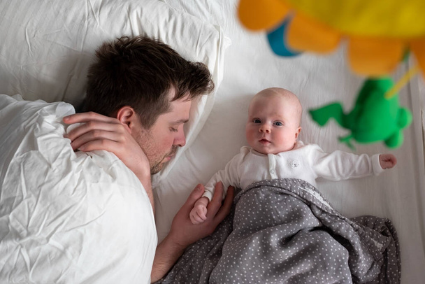 Κοιμώμενος πατέρας και χαριτωμένο παιδί αναπαύονται μαζί στο κρεβάτι. - Φωτογραφία, εικόνα