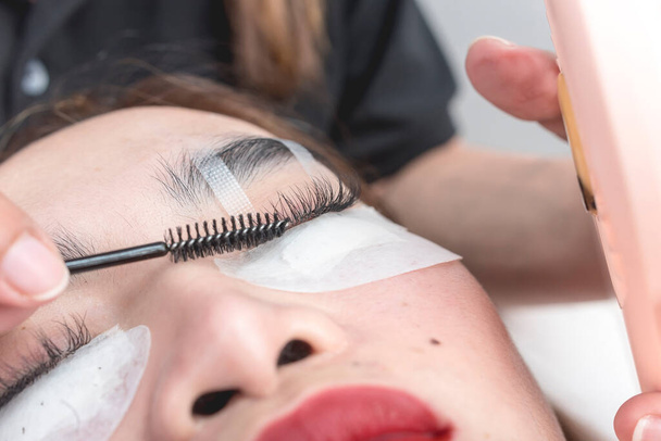 A beautician uses a lash roller to style the eyelash extensions of a customer. - Foto, imagen