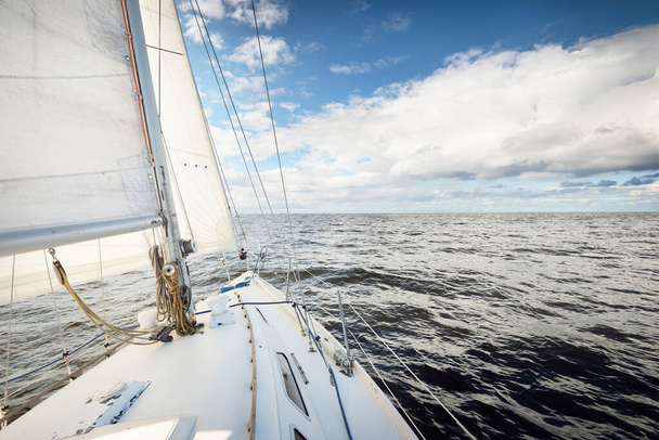 Bílá šalupa upravená jachta plachtění na otevřeném moři za jasného dne. Pohled z paluby na příď. Kumulus mraků. Doprava, cestování, plavba, sport, rekreace, volný čas, závodní, regata - Fotografie, Obrázek
