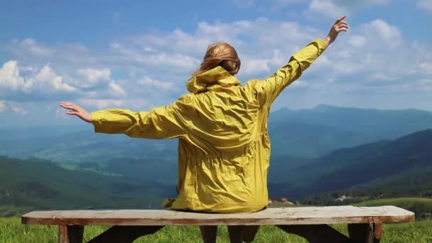 Matkustava nainen patikoija nostaa kätensä istuu vuoren kalliolla kesällä aurinkoinen päivä. Kaunis vuoristomaisema - Materiaali, video