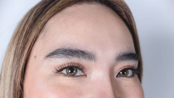 Szoros kép egy 20-as éveiben járó filippínó nő homlokáról és szeméről. Szempilla-hosszabbítóval és borostyán kontaktlencsével. - Fotó, kép
