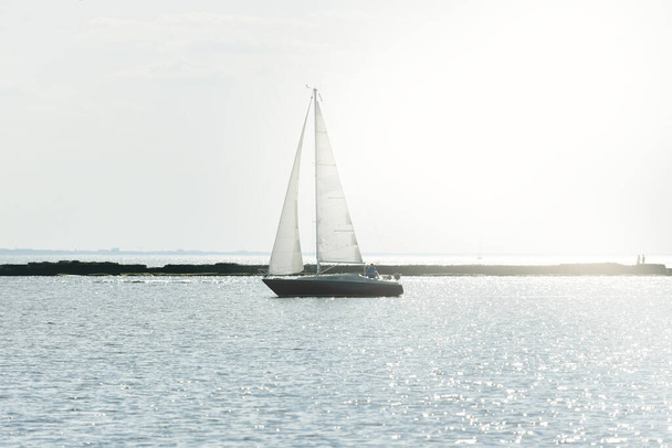 Sloop bianco barca truccata vela nel Mar Baltico al tramonto. Cielo limpido dopo la tempesta, luce solare soffusa. Faro. Trasporti, viaggi, crociera, sport, ricreazione, attività ricreative, corsa, regata - Foto, immagini