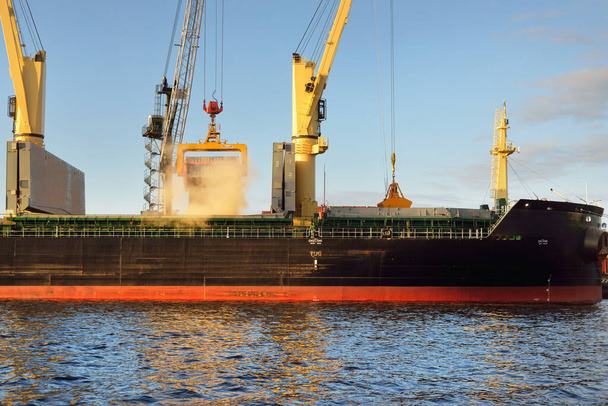 Groot vrachtschip (bulkcarrier, 179 meter lengte) met kranen in de haventerminal. Oostzee. Goederenvervoer, logistiek, wereldwijde communicatie, economie, bedrijfsleven, industrie, levering - Foto, afbeelding