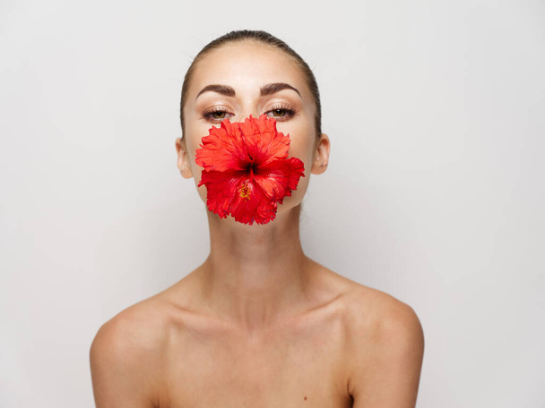 mooie vrouw met rode bloem in mond bijgesneden bekijk licht achtergrond - Foto, afbeelding