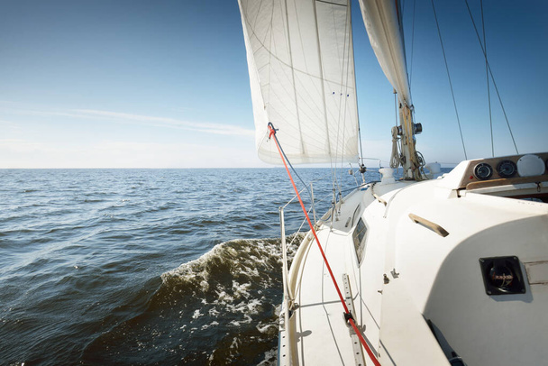 Sloop blanc gréé yacht naviguant dans la mer Baltique au coucher du soleil. Vue d'un cockpit à l'avant, mât et voiles. Transport, voyage, croisière, sport, loisirs, activité de loisirs, régate - Photo, image