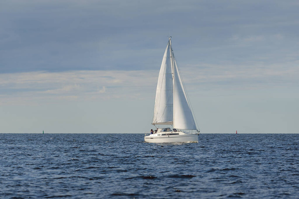 Fehér sloop manipulált jacht vitorlázás a Balti-tengeren naplementekor. Tiszta ég a vihar után, lágy napfény. Közlekedés, utazás, sétahajózás, sport, rekreáció, szabadidős tevékenység, verseny, regatta - Fotó, kép