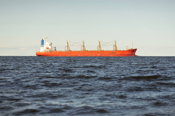 Gran granelero rojo (179 metros de longitud) navegando en un mar Báltico abierto. Cielo dramático. Transporte de mercancías, embarcación náutica, logística, comunicaciones globales, economía, negocios, industria - Foto, Imagen