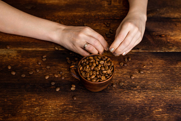 Coffee beans full cup and female hands on brown old wooden background. - Fotó, kép