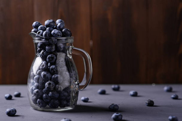 Blueberries in a glass jug on a gray concrete background. The benefits of berries, vegetarianism concept. - Φωτογραφία, εικόνα