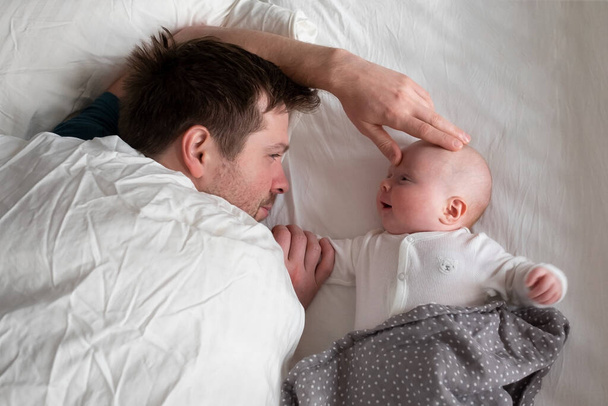 Κοιμώμενος πατέρας και χαριτωμένο παιδί αναπαύονται μαζί στο κρεβάτι. - Φωτογραφία, εικόνα