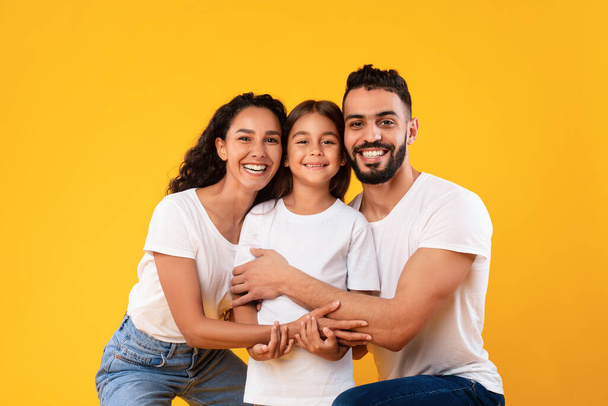Happy Middle-Eastern Parents Hugging Their Kid Daughter On Yellow Background - Фото, изображение