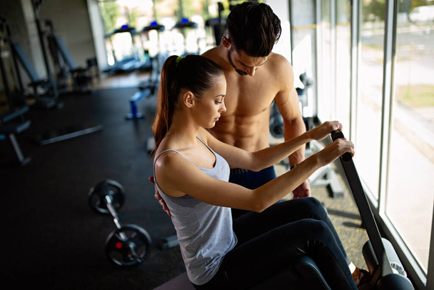 Young man personal trainer helping woman to working out in gym. Healthy lifestyle sport people concept - Foto, afbeelding