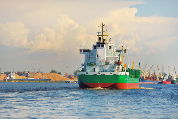 Büyük yeşil yük gemisi gün batımında kargo terminaline varacak. Arka planda gemiler ve vinçler var. Dramatik bulut manzarası. Yük taşımacılığı, küresel iletişim, endüstri, ekonomi, lojistik - Fotoğraf, Görsel