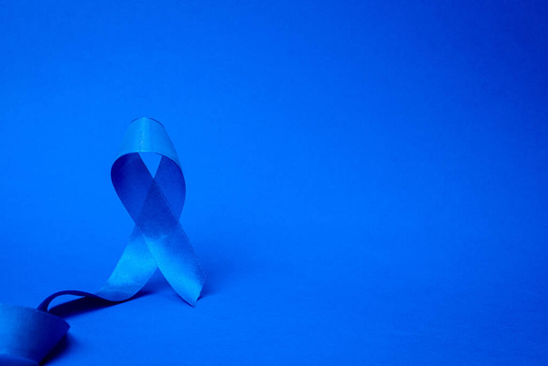 リボン癌。深い青色の背景に隔離された青い前立腺がんのリボンで11月の男性の健康の意識。副腎皮質がんの概念. - 写真・画像