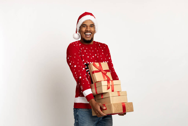 Noel Baba şapkalı mutlu siyah adam elinde hediyeler tutuyor. - Fotoğraf, Görsel
