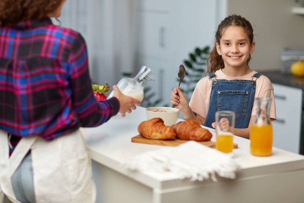 Hymyilevä pieni tyttö näyttää peukalot, joilla on terve aamiainen yhdessä äidin kanssa keittiössä. - Valokuva, kuva