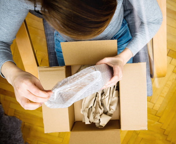 Vista aérea de la mujer curiosa unboxing en la sala de estar nueva entrega de productos pedidos de comercio electrónico a través de interne - Foto, imagen