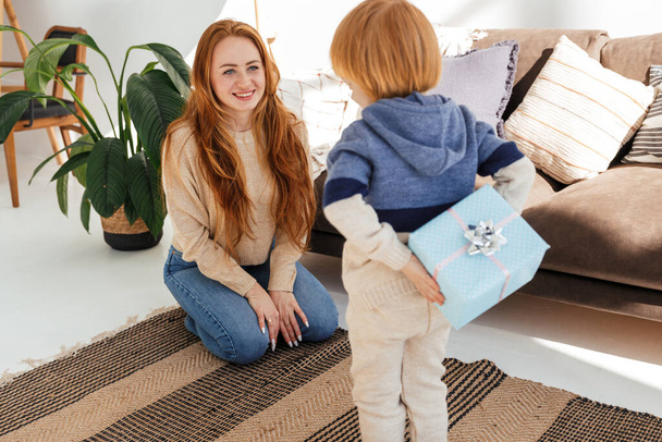 Little cute red haired boy gives mom a new year gift - Foto, afbeelding