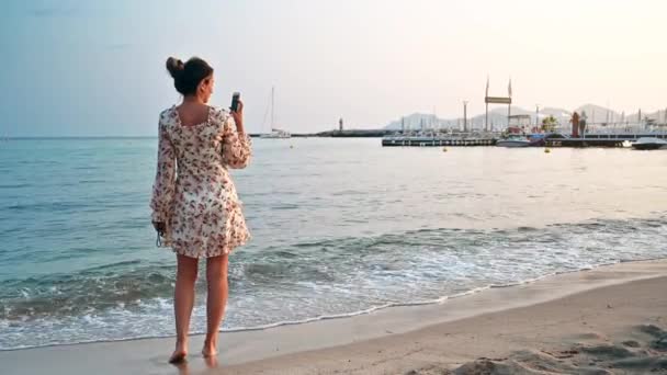 Блондинка снимает на смартфон на пляже на побережье Средиземного моря в Каннах, Франция на закате - Кадры, видео