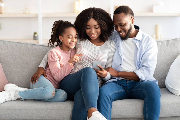 Boldog afro-amerikai család tartja és használja a mobiltelefon otthon - Fotó, kép