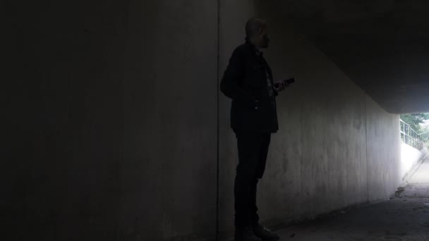 Shady Bald Ethnic Minority Checking Mobile Waiting In Underpass Tunnel, Looking Side To Side. Verrouillé, Angle bas - Séquence, vidéo