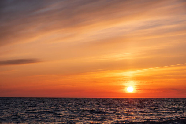 avondlucht boven de zee, besmeurde wolken in de avondlucht. de ondergaande zon aan de oranje hemel - Foto, afbeelding