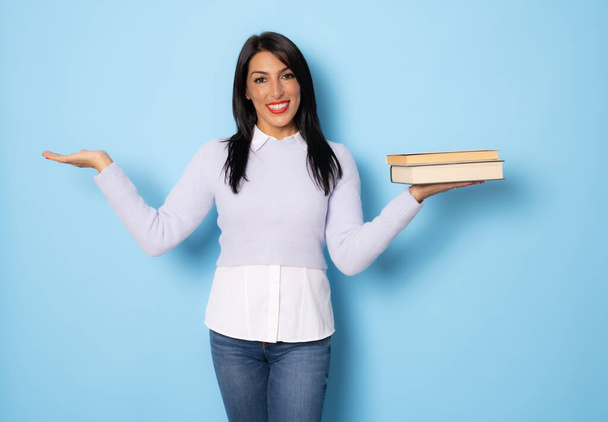 Portrait of a smiling pretty woman holding books and looking at camera isolated over blue background - Foto, Imagen
