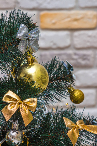 Kerstcompositie, gouden en zilveren kerstballen, strikken, dieren, klokken, verlichte bloemenslingers op een feestelijke kerstboom tegen de decoratieve antieke bakstenen muurachtergrond. Begrepen-ruimte. Wintervakantie concept - Foto, afbeelding