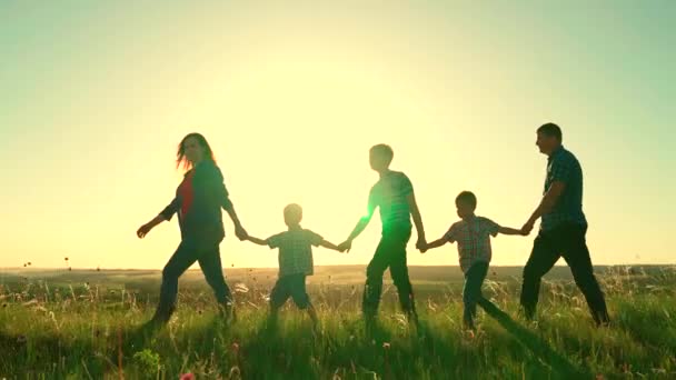silhouet van gelukkige familie bij zonsondergang, kleine kinderen met de hand, kinderdroom, kinderen met ouders op vakantie reizen, jongens met hun vader en moeder in de zon, hou van mama en papa, actieve wandeling - Video