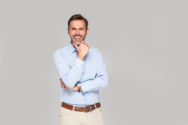 Photo of a smiling formal business man wearing a light blue shirt,  standing and looking at camera against gray studio background. - Photo, image