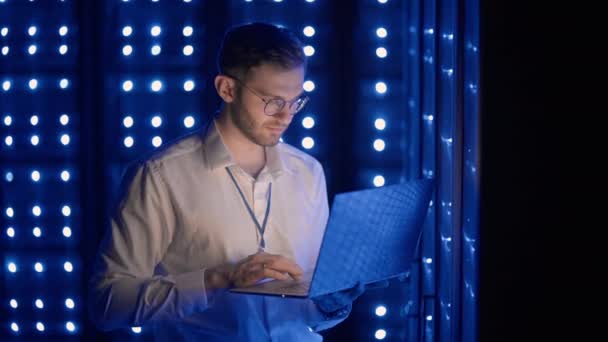 προσωπογραφία του ανθρώπου που εργάζεται σε αίθουσα διακομιστή με φορητό υπολογιστή. τεχνικός κάνει τσεκ-απ στο δωμάτιο του σέρβερ. Καυκάσιος μηχανικός με γκρι σακάκι εργάτη - Πλάνα, βίντεο