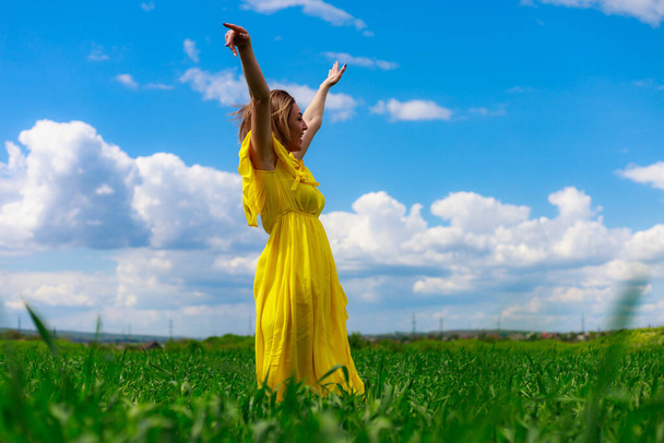 Młoda kobieta w żółtej sukience na zewnątrz, na zielonym polu. Taniec jako symbol szczęścia i dobrego nastroju - Zdjęcie, obraz