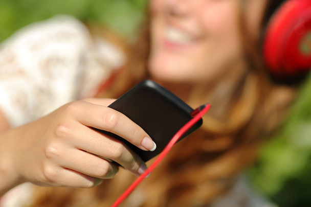 Mujer mano usando un teléfono inteligente para escuchar la música con auriculares
 - Foto, Imagen