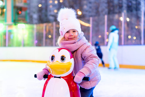 A little girl is skating on an ice rink, holding on to a support, a child is learning to skate, winter entertainment for children. - Photo, Image