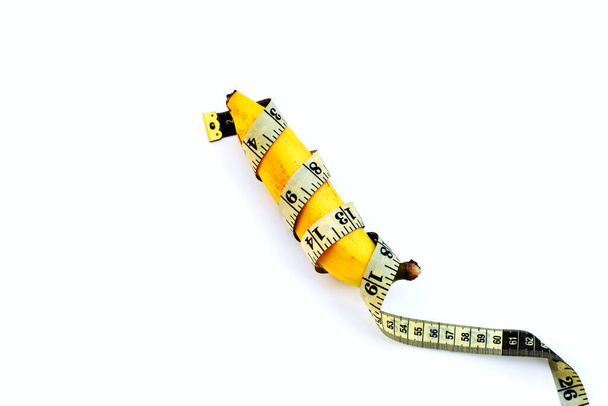 Banana wrapped in measuring tape on white background. - Photo, Image
