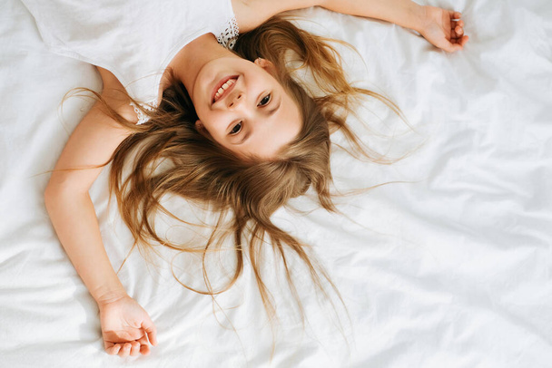 Pieni tuhma iloinen tyttö koulutyttö aamulla valoisassa huoneessa valkoisella taustalla makuuhuone grimaces hymyilee ympäri ja kasvot - Valokuva, kuva