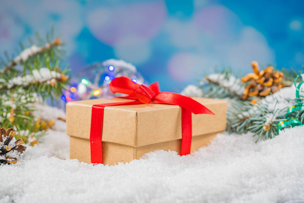 Coffret cadeau artisanat décoratif avec arc rouge debout dans la neige fraîche sur un fond de Noël bokeh - Photo, image